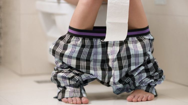 A person on the toilet with a roll of toilet paper, depicting a typical restroom setting.
